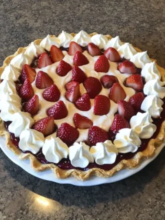 A fresh strawberry pie with a flaky crust, glossy strawberry glaze, and whipped cream, garnished with graham cracker crumbs.