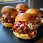 Close-up of delicious BBQ Pulled Pork Sliders with vibrant coleslaw on a dark slate.