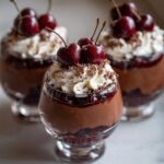 Three elegant Black Forest Mousse Cups topped with whipped cream, chocolate shavings, and fresh cherries.