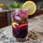 A tall glass filled with Blackberry Mint Lemonade, packed with ice, fresh blackberries, mint leaves, and lemon slices.