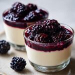 Close-up of two glasses filled with creamy Blackberry Vanilla Bean Panna Cotta topped with fresh blackberries and berry sauce.