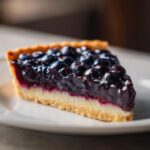 A delicious slice of Blueberry Lemon Curd Tart on a white plate, showcasing the flaky crust, creamy filling, and fresh blueberries.