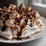 A close-up of a decadent Chocolate Hazelnut Pavlova, topped with whipped cream, chocolate shavings, and chopped hazelnuts.