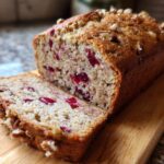 A close-up of a slice of moist Cranberry Walnut Bread, showcasing plump cranberries and crunchy walnuts.