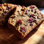 A close-up view of a slice of moist Cranberry Walnut Bread, showcasing the texture and visible cranberries and walnuts.