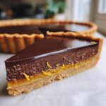 A slice of Dark Chocolate Orange Tart with a glossy chocolate ganache and bright orange filling.