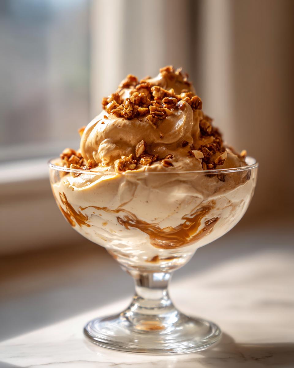 A decadent serving of Hazelnut Praline Mousse in a glass dish, topped with crunchy praline pieces and drizzled with caramel.