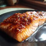 Close-up of a glistening Honey Garlic Glazed Salmon fillet on a dark plate, showing flaky texture and rich glaze.