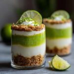 Close-up of layered Key Lime Parfaits in a glass, featuring creamy white and vibrant green layers with a graham cracker crust and lime garnish.