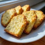 Close-up of golden-brown Lemon Lavender Shortbread slices arranged on a white plate, with visible herbs and zest.