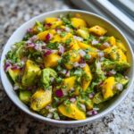A close-up of a bowl filled with vibrant Mango Avocado Salsa with Lime, featuring chunks of mango, avocado, red onion, and cilantro.