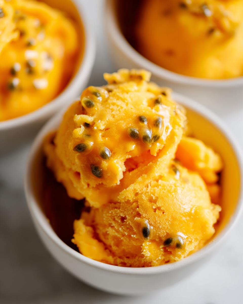 Close-up of bright orange Mango Passionfruit Sorbet in white bowls, topped with passionfruit seeds.