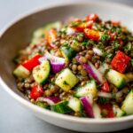 Close-up of a vibrant Mediterranean Lentil Salad with chopped cucumber, red onion, tomatoes, and fresh herbs.