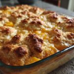 Close-up of a freshly baked Peach Bourbon Cobbler in a glass baking dish, with golden brown biscuit topping.