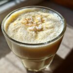A close-up of a frothy Pineapple Coconut Smoothie topped with shredded coconut.