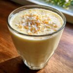 A close-up of a glass filled with a creamy Pineapple Coconut Smoothie, topped with toasted coconut flakes.