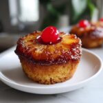 Close-up of a moist Pineapple Upside Down Cupcake topped with a caramelized pineapple ring and a bright red cherry.