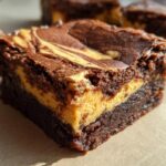 Close-up of a rich chocolate brownie with a distinct swirl of pumpkin cheesecake filling.