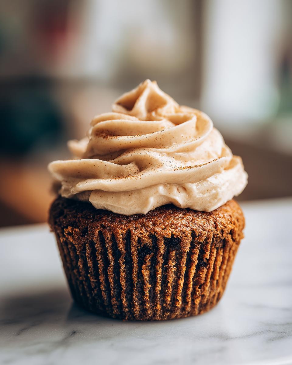 A close-up of a single Pumpkin Spice Latte Cupcake topped with swirled frosting and a dusting of cinnamon.