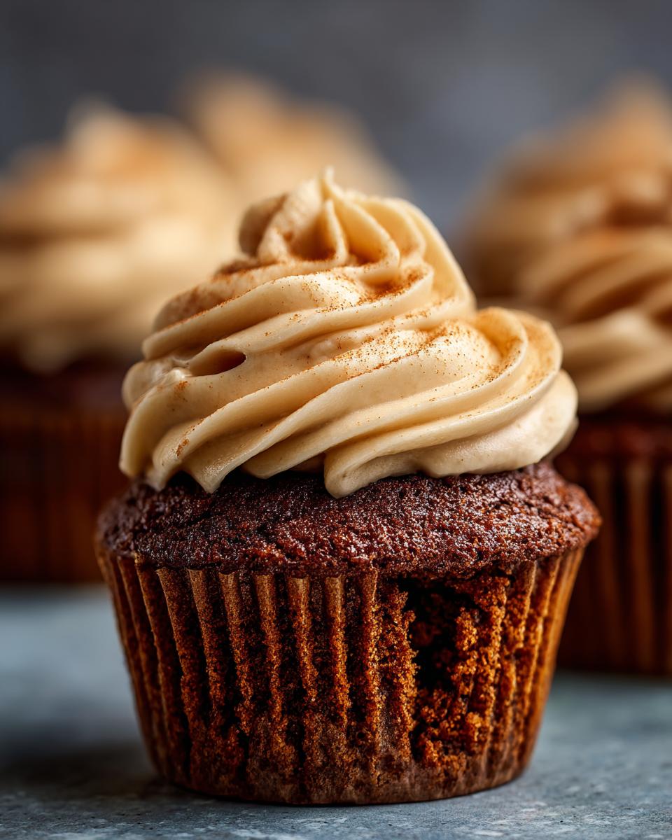 Close-up of a decadent Pumpkin Spice Latte Cupcake topped with creamy frosting and a sprinkle of cinnamon.