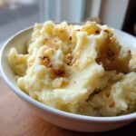 A close-up of creamy Roasted Garlic Mashed Potatoes topped with crispy garlic bits.