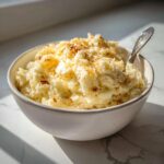 A bowl of creamy Roasted Garlic Parmesan Mashed Potatoes topped with parmesan and herbs, with a spoon.