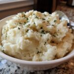 A close-up of a bowl filled with fluffy Roasted Garlic Parmesan Mashed Potatoes, garnished with fresh parsley.