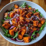 A vibrant bowl of Roasted Sweet Potato Salad featuring chunks of sweet potato, red onion, dried cranberries, and pecans on a bed of greens.