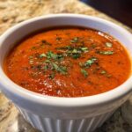 A close-up of a bowl of vibrant Roasted Tomato Basil Soup, garnished with fresh basil.