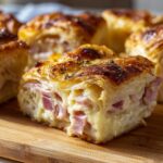 A close-up of a slice of Savory Ham and Cheese Croissant Bake, showcasing flaky pastry, diced ham, and melted cheese.