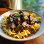 A bowl of Slow Cooker Beef Stroganoff served over egg noodles, garnished with fresh parsley and mushrooms.