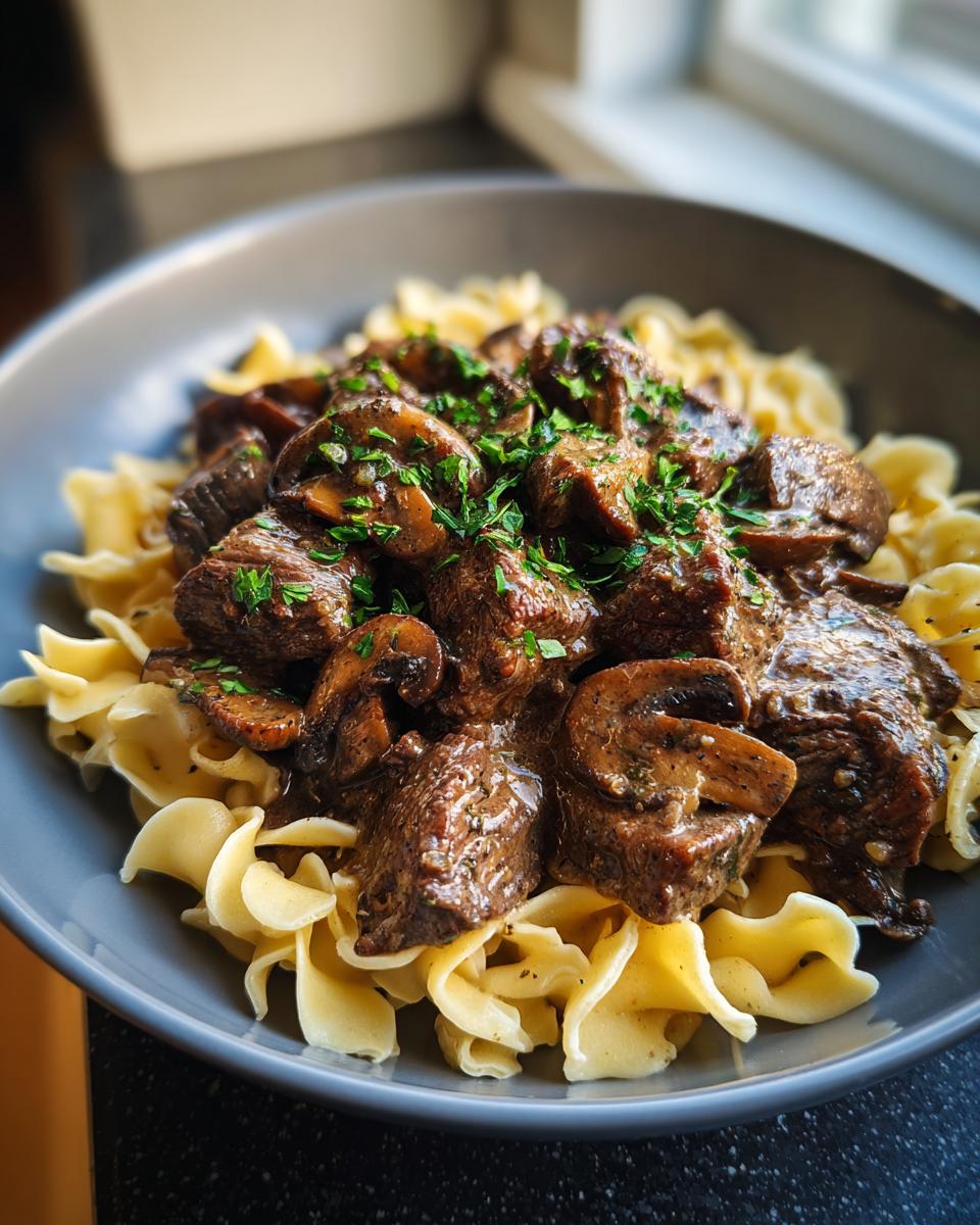 A close-up of Slow Cooker Beef Stroganoff served over egg noodles, topped with fresh parsley.