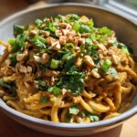 A close-up of a bowl filled with delicious Spicy Thai Peanut Noodles, garnished with chopped peanuts, cilantro, and green onions.