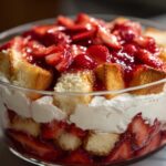 Close-up of a layered Strawberry Shortcake Trifle in a glass bowl, featuring pound cake, whipped cream, and fresh strawberries.