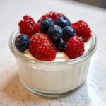 A close-up of a creamy Vanilla Bean Panna Cotta topped with fresh strawberries, blueberries, and raspberries.