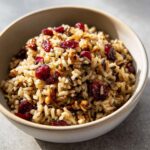 A close-up of a bowl filled with Wild Rice Pilaf with Cranberries and toasted nuts.
