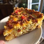 A close-up of a slice of Bacon Onion Tomato Pie, showcasing crispy bacon, sweet tomatoes, and tender onions in a flaky crust.