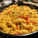 A close-up view of a Cheesy Cajun Chicken Rotini Skillet, featuring rotini pasta coated in a creamy cheese sauce with chunks of chicken and diced bell peppers.
