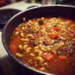 Close-up of a pot filled with Comforting Hamburger Soup With Macaroni, featuring elbow pasta, ground beef, and diced carrots.