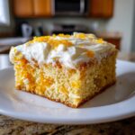 A close-up of a slice of easy Creamsicle Cake, topped with white frosting and orange zest.