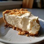 A delicious slice of easy no bake cheesecake with a graham cracker crust and creamy filling, topped with crumbs.
