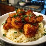 A bowl of creamy parmesan rice topped with glistening honey garlic chicken bites and garnished with fresh chives.