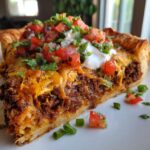 A delicious slice of Irresistible Mexican Pizza Recipe, topped with seasoned ground beef, melted cheese, sour cream, pico de gallo, and cilantro.