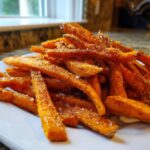 A close-up of a pile of Irresistible Sweet Potato Fries, seasoned with spices and sea salt, on a white plate.