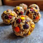 Close-up of several homemade Monster Cookie Balls, packed with oats, chocolate chips, and colorful candy pieces.