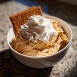 A bowl of creamy Pumpkin Cheesecake Dip topped with whipped cream and a graham cracker.