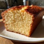 A close-up of a moist and golden-brown slice of Slap Ya Momma Pound Cake on a white plate.