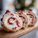 Close-up of three slices of Turkey Cranberry Pinwheels on a wooden board, showcasing the creamy filling and cranberry swirl.