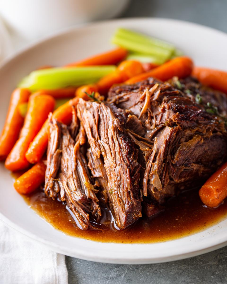 Close-up of a tender Ultimate Slow Cooker Pot Roast Recipe with carrots and celery on a white plate.