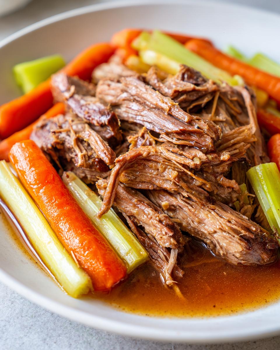 Close-up of tender shredded beef from the Ultimate Slow Cooker Pot Roast Recipe, served with carrots and celery.